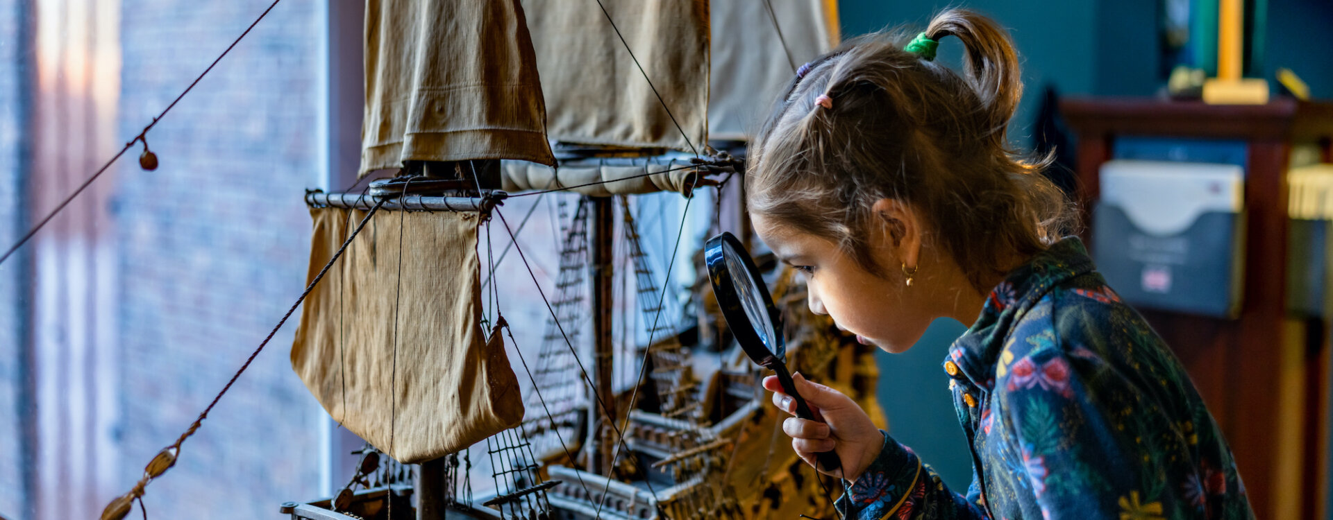 Meisje kijkt met vergrootglas naar modelschip 17e eeuw
