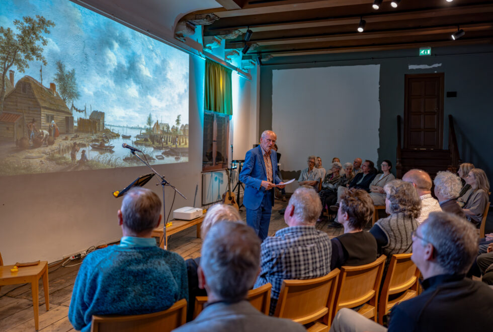 Persoon spreekt zaal met mensen toe met daarachter projectie van schilderij